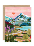 The Spectacular Year Luxe Birthday Card by Biely & Shoaf is an A2 card with snowy mountains, purple flowers, a pink-orange sky, and gold foil accents highlighting “Wishing you a spectacular year” and “Happy Birthday.”.