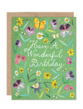 The Violet Petals Luxe Birthday Card by Biely & Shoaf is a green A2 eco-friendly card with painted flowers, leaves, butterflies, and bees. "Have A Wonderful Birthday" appears in white script, with a brown envelope partially visible behind.