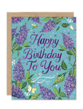 The Lilacs Luxe Birthday Card by Biely & Shoaf features "Happy Birthday To You" in purple on blue with lilacs, leaves, butterflies, and stars—an eco-friendly A2 Luxe Collection greeting card for stationery lovers.