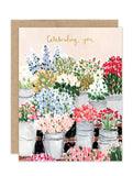 The Flower Market - Luxe Birthday Card by Biely & Shoaf features "Celebrating you" in gold script above illustrated buckets of colorful flowers on a soft pink background, from the A2 Luxe Collection’s elegant gold foil greeting cards.