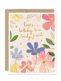 The Rainbow Flowers Luxe Birthday Card by Biely & Shoaf features watercolor flowers in pink, blue, and yellow with green leaves. Gold foil text reads "happy birthday to a lovely friend," surrounded by small gold hearts.