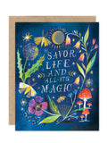 The Savor Life Luxe Birthday Card from Biely & Shoaf features a gold foil design on blue, with vibrant flowers, mushrooms, butterflies, and dandelions surrounding the hand-lettered message: “Savor life and all its magic.”.