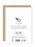 The back of the Pink Rose Luxe Anniversary Card by Biely & Shoaf shows a leaf illustration, artist bio, brand logo, copyright, green icons, and barcode. A brown envelope is partially visible behind this eco-friendly A2 card.