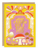 The Rare Find Mushroom Friendship Card by Biely & Shoaf features gold foil, a yellow border, stylized mushrooms, stars, and a colorful sunset. The front reads “GOOD FRIENDS ARE A RARE FIND” in bold retro letters. Illustrated by Carrie Shryock.