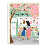 The Patisserie Mother's Day Card by Biely & Shoaf features Emma Block’s illustration of a woman and child outside a bakery, with pink blossoms and a “Happy Mother’s Day” banner inside. Printed in the USA.