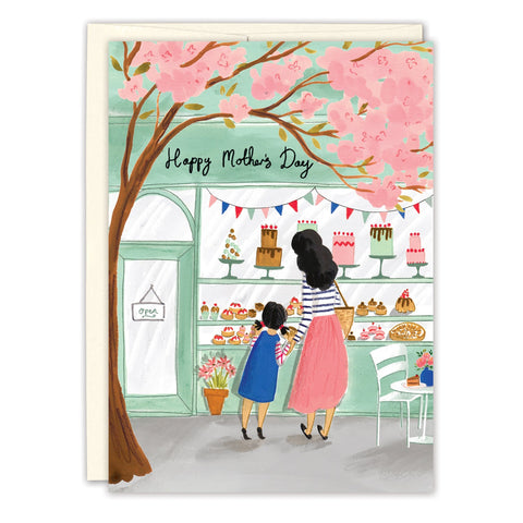 The Patisserie Mother's Day Card by Biely & Shoaf features Emma Block’s illustration of a woman and child outside a bakery, with pink blossoms and a “Happy Mother’s Day” banner inside. Printed in the USA.