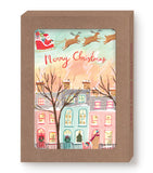 Santa flies at sunset above snowy homes on Biely & Shoaf’s Santa In Flight Holiday Card Set—gold foil, “Merry Christmas.”.