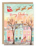 Biely & Shoaf’s Santa In Flight card shows Santa’s sleigh over colorful homes, printed on recycled paper.