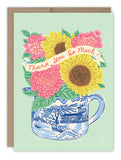 The Bright Florals Vase Thank You Card by Biely & Shoaf features pink and yellow flowers in a blue and white vase, a Thank You So Much! ribbon, light green background, and comes with a brown envelope. Blank inside.