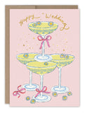 The Champagne Tower Happy Wedding Card by Biely & Shoaf features champagne glasses stacked in a pyramid with floral designs and pink ribbons on a pink background. Gold text reads Happy Wedding, accented with sparkles, like a gold foil card.