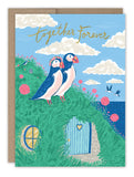 The Seaside Puffins Anniversary Card by Biely & Shoaf features two puffins with flower crowns on a grassy hill. Birds fly above the sea, with “together forever” in script—an eco-friendly, charming card perfect for anniversaries.