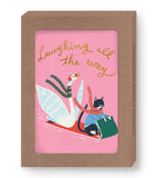 The Laughing All The Way Boxed Holiday Cards by Biely & Shoaf feature a goose and cat in scarves on a green sled with “Laughing all the way” in gold foil on pink. Packaged in a brown box, these holiday cards are printed on recycled paper.
