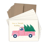The Biely & Shoaf Tree-rific Penguin In Truck Boxed Holiday Cards set includes 10 cards featuring a pink truck with penguins and Christmas trees, Have a treerrific holiday! text, plus brown recycled paper envelopes.
