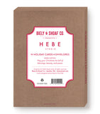 A brown box labeled Biely & Shoaf presents All Is Calm Snowy Village Boxed Holiday Cards, including 10 Christmas cards and envelopes. The label features a gold foil holiday message with company info in red and white text.