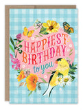 The Gingham Happiest Birthday Card by Biely & Shoaf features a blue gingham background with flowers, butterflies, and a yellow bird. “Happiest Birthday to you” stands out in pink and blue on recycled paper in Katie Daisy’s cheerful style.