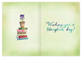 The Storybook Enchanted Birthday Card by Biely & Shoaf features a potted purple flower on colorful books, with “Wishing you a storybook day!” in blue and teal script on pale green recycled paper for an eco-friendly touch.