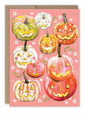 The Pumpkins Halloween Card by Biely & Shoaf features cheerful jack-o’-lanterns in orange, white, green, and pink on a pink floral background—printed on recycled paper for an eco-friendly touch.