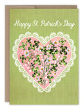 The Clover Heart St. Patrick's Day Card by Biely & Shoaf features "Happy St. Patrick’s Day" above a pink heart with clovers and daisies, outlined in white lace on a textured green background—printed in the USA.