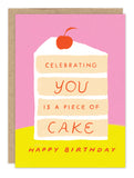 The Piece of Cake Birthday Card by Biely & Shoaf features a slice of cake with a cherry on a pink and yellow background. The front reads “Celebrating you is a piece of cake,” and below, “Happy Birthday.” Printed in the USA.