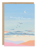 The Biely & Shoaf Many Moons Anniversary Card features a pastel landscape with hills, clouds, flying birds, a crescent moon, and handwritten "love you now & many moons more"—ideal for anniversaries.