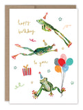 The Biely & Shoaf Leaping Frogs Birthday Card features three party hat-wearing frogs, a stack of balloons, a gift, and cheerful happy birthday to you text, with festive stars and swirls decorating the background.