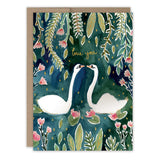 Two white swans face each other on a dark green background with leaves and pink flowers. "Love you" appears in gold foil above them on the front of this Biely & Shoaf Swans Love Card.