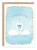 The Biely & Shoaf Swans On Your Wedding Day Card features two swans forming a heart, a pink heart above them, floral borders, and "on your wedding day" in pink cursive—an elegant choice to celebrate newlyweds.