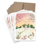 The Biely & Shoaf Red Sky Cozy Christmas Boxed Holiday Cards feature a snowy village under a pink-orange sky and come with brown envelopes. Made from recycled paper, each card reads “Warm and cozy Christmas wishes.”.