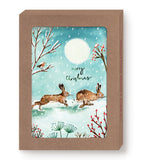 Two bunnies frolic in snow under a full moon on Biely & Shoaf’s Bunnies Merry Christmas Holiday Card Set.