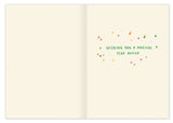 The Rainbow Candles Birthday Card by Biely & Shoaf features “Wishing you a magical year ahead” in green, surrounded by colorful confetti on the right; the left page is blank. Printed on recycled paper.