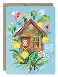 The "Home Sweet Home Card" by Biely & Shoaf showcases a charming illustration of a quaint house surrounded by vibrant flowers and foliage, conveying warm wishes. A bright yellow bird perches on the roof, while "Home Sweet Home" is elegantly written on the right side against a light blue background, welcoming positivity.