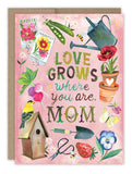 This Mother's Day, surprise your mom with the Biely & Shoaf "Love Grows Mother's Day Card." Illustrated by Katie Daisy on recycled paper, this card showcases delightful illustrations of flowers, a watering can, garden tools, a birdhouse, and butterflies. The interior features the heartfelt message: "Love grows where you are, Mom," surrounded by vibrant flowers and seeds against a pink background.