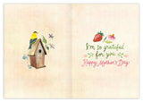 The Love Grows Mother's Day Card by Biely & Shoaf, illustrated by Katie Daisy, showcases a charming birdhouse and a yellow bird amidst floral designs on the left side. On the right, heartfelt words of appreciation are beautifully paired with illustrations of a strawberry and flower, all elegantly printed on recycled paper.